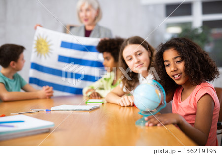 Female teacher showing uruguayan flag to kids in geography class Female teacher showing uruguayan flag to kids in geography class 136219195