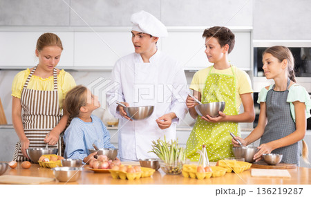 Friendly young chef running culinary courses for group of children 136219287