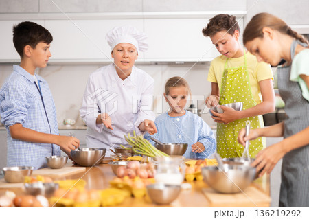 Adult woman cook teaches to cook group of children Adult woman cook teaches to cook group of children 136219292