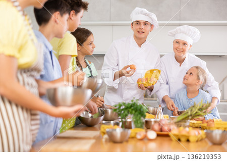 Positive professional chefs in white uniform conducting culinary masterclass for tweens 136219353