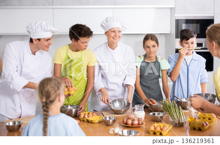 Amiable male and female chefs in white uniform running culinary courses for children Amiable male and female chefs in white uniform running culinary courses for children 136219361