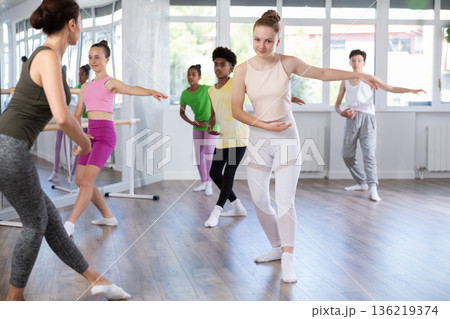 Positive teenage girl practicing ballet positions standing in row with others 136219374