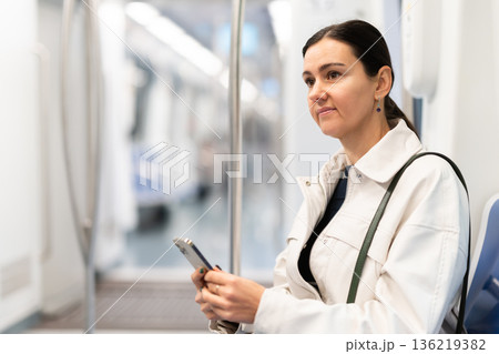 European woman sitting on seat in subway train and using smartphone European woman sitting on seat in subway train and using smartphone 136219382