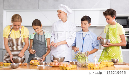 Adult woman cook teaches to cook group of children Adult woman cook teaches to cook group of children 136219466