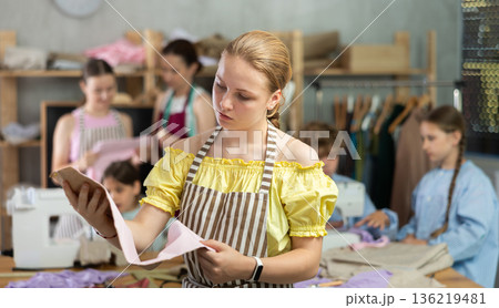 Portrait of a happy girl with a pattern and fabric in her hands during sewing lesson 136219481