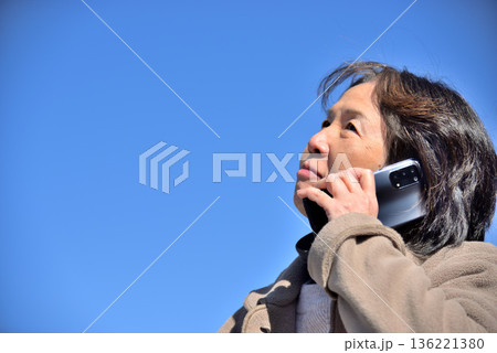 青空の下 携帯電話で通話するシニア女性 136221380