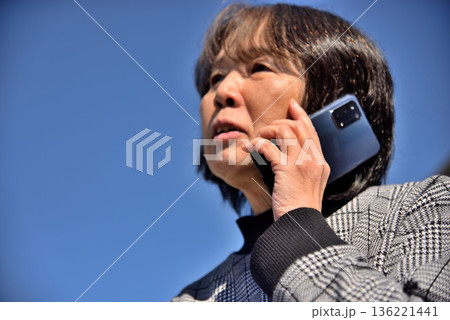 青空の下 携帯電話で通話するシニア女性 136221441