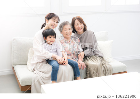 逆光の綺麗な部屋で祖母と母と子ども(ひ孫）が笑顔で抱き合う四世代家族、親子の幸せな記念写真 136221900