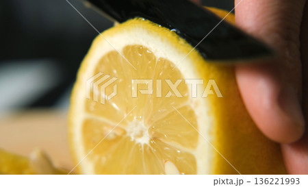 Macro close-up of slicing lemon with knife on board, showing juicy texture and color. Healthy vitamin and freshness concept  136221993