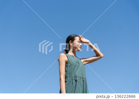 青空の下で眩しそうにする女性 136222666
