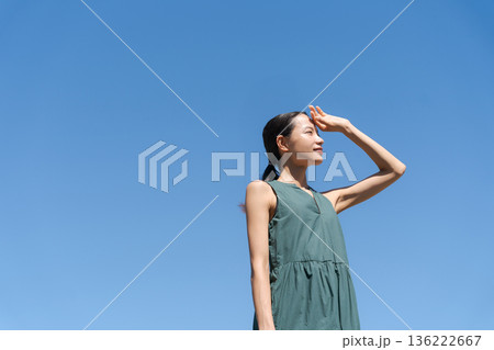 青空の下で眩しそうにする女性 136222667