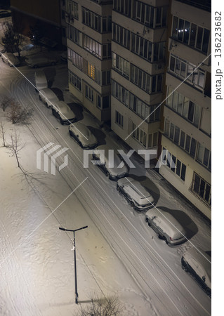 Lviv Ukraine 01.01.26 Snow covers cars on a quiet street near an apartment building at night 136223682