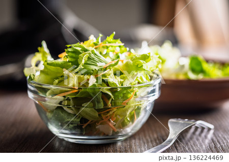 Mix of fresh green salad with carrot in bowl on wooden table. Mix of fresh green salad with carrot in bowl on wooden table. 136224469