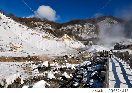 冬晴れの「登別地獄谷」雪と茶色い山肌の中を谷の中心部へと伸びる遊歩道 136224818