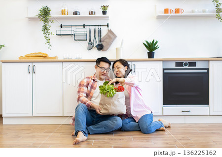 A happy couple unpacks a bag of fresh groceries in their bright, modern kitchen 136225162