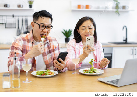 An Asian couple enjoys a healthy meal while simultaneously using their smartphones, possibly for work or social media 136225209