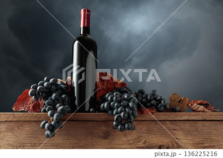 Red wine bottle with blue grapes on an old wooden table. 136225216