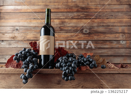 Red wine bottle with blue grapes on an old wooden table. Red wine bottle with blue grapes on an old wooden table. 136225217