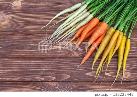 Yellow, orange and white carrots on the brown wooden table. 136225449