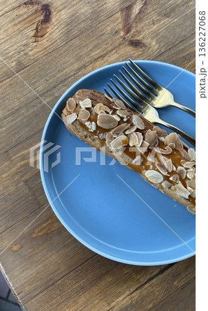 Uncut almond pastry topped with sliced almonds, placed on a vibrant blue plate with two forks beside it. Uncut almond pastry topped with sliced almonds, placed on a vibrant blue plate with two forks beside it. 136227068