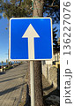Blue rectangular one way arrow sign directs vehicles along a seaside street, captured on a bright sunny day.  136227076