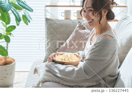 リビングのソファに座りポップコーンを食べる笑顔のアジア人女性 136227445