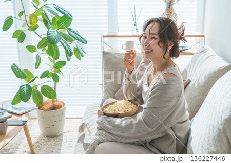 リビングのソファに座りポップコーンを食べる笑顔のアジア人女性 136227446