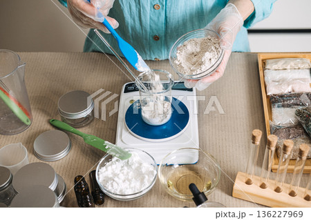 Hands holding small glass bowl pour powder into beaker positioned on digital scale. raw beauty ingredients, skincare transparency, minimalist formulation, natural cosmetic components. 136227969