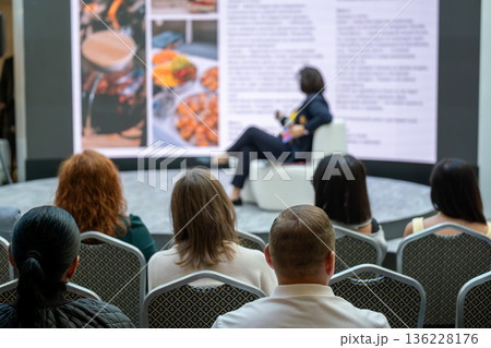 Audience watching a speaker during a presentation at a conference and learning from experts Audience watching a speaker during a presentation at a conference and learning from experts 136228176