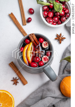 A cup of red mulled wine with cinnamon, orange and cranberry on a light background 136228917