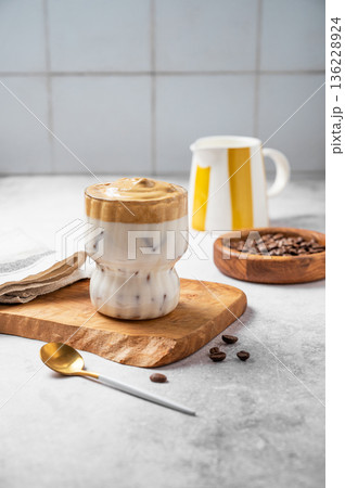 Iced Dalgona coffee on a wooden board on a kitchen blue tile background with milk jug 136228924