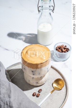 Dalgona coffee on a marble background with bottle, coffee beans, spoon and morning shadow Dalgona coffee on a marble background with bottle, coffee beans, spoon and morning shadow 136228927