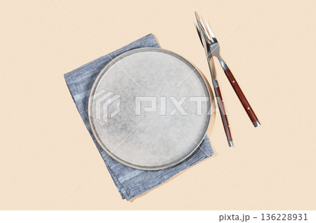A ceramic plate with a linen napkin and cutlery on a yellow isolated background. 136228931