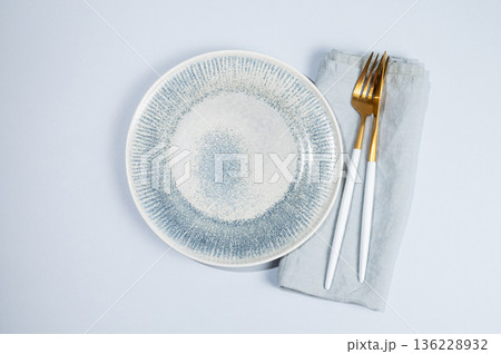 A ceramic blue plate with a linen napkin and cutlery on a light isolated background. 136228932