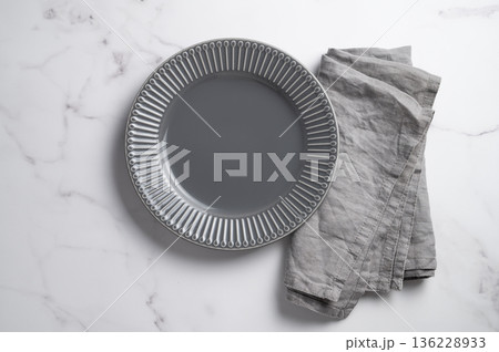 A ceramic dark gray plate with a linen napkin on a marble background. A ceramic dark gray plate with a linen napkin on a marble background. 136228933