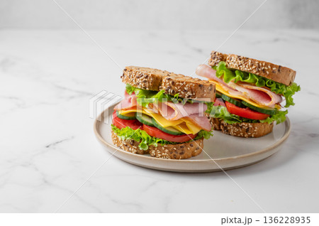 Two sandwiches with ham, cheese, lettuce, vegetables and seeded bread on a plate 136228935