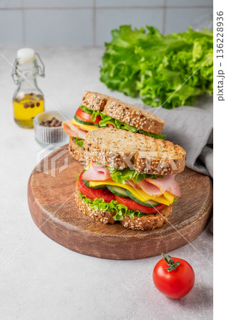Two sandwiches with ham, cheese, lettuce and vegetable on a wooden board on a concrete background Two sandwiches with ham, cheese, lettuce and vegetable on a wooden board on a concrete background 136228936
