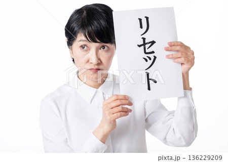 リセットと書かれた紙を持ち口をとがらせる白いシャツを着たシニア女性 136229209