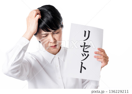 リセットと書かれた紙を持ち頭を抱えるシニア女性 136229211