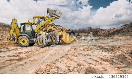 A construction site or sand pit with two powerful wheeled front loaders ready to go, under partly cloudy skies during the day 136229593