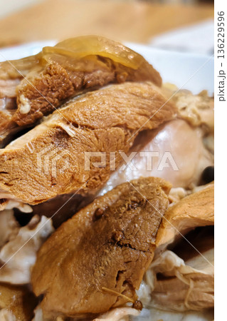 A bowl holds slices of cooked chicken placed with other food items on a wooden table. The meal is ready for serving and eating 136229596