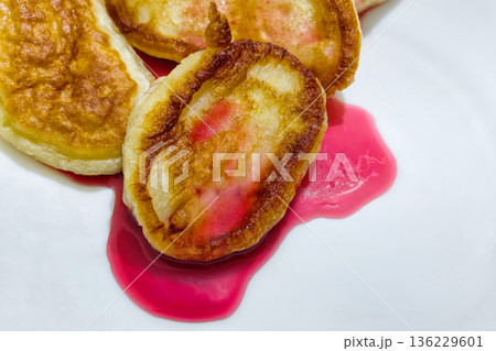 Pancakes sit on a white plate with red syrup pooled around them, ready to be eaten at breakfast or brunch with a focus on food presentation 136229601