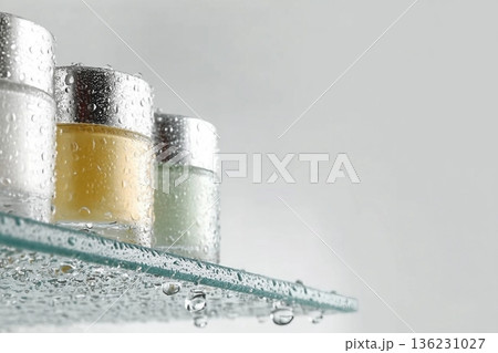 Glass tubes of cosmetic product with serum and cream on a glass shelf and water drops on a white background, bottom view. Skin care concept 136231027