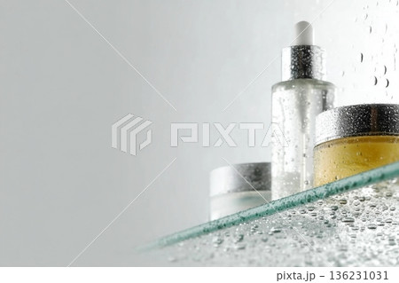 Glass tubes of cosmetic product with serum and cream on a glass shelf and water drops on a white background, bottom view. Skin care concept 136231031