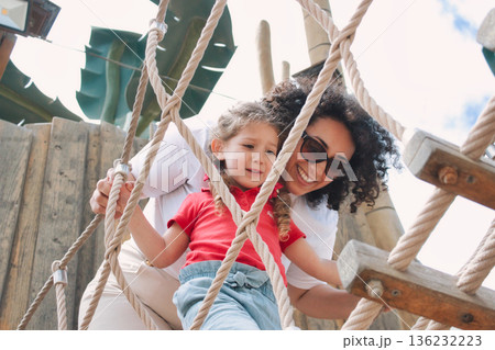 A cheerful mother encouraging her daughter playing together on a rope ladder in a public park - encouragement concept A cheerful mother encouraging her daughter playing together on a rope ladder in a public park - encouragement concept 136232223