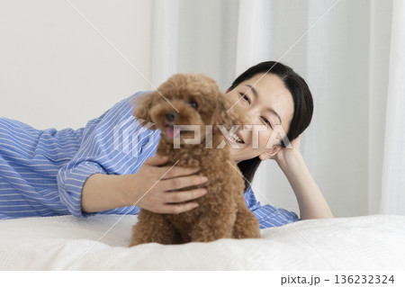 ベッドに横になって愛犬（トイプードルの5歳の男の子）を撫でるミドル女性 136232324