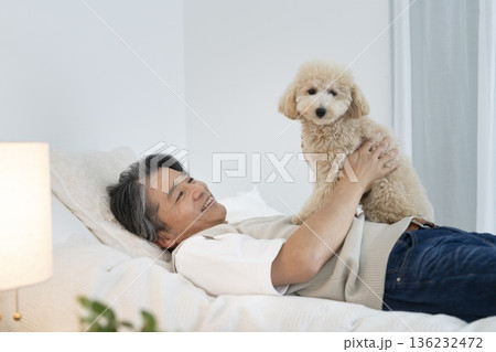 ベッドに寝ながら愛犬を抱っこする50代の男性 136232472
