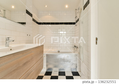 A sleek and contemporary bathroom featuring white tiled walls, a wooden vanity, and stylish black and white flooring. Perfect for design inspiration and home decor ideas. A sleek and contemporary bathroom featuring white tiled walls, a wooden vanity, and stylish black and white flooring. Perfect for design inspiration and home decor ideas. 136232551