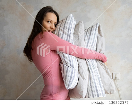 woman holds pile of pillows in her hands. pillows are in different colors, look like stack.  136232575