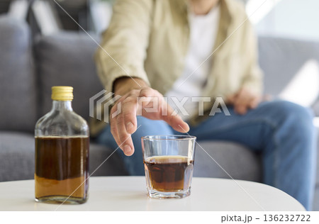 Man drinking whiskey on couch, reflecting alcohol addiction and health risks Man drinking whiskey on couch, reflecting alcohol addiction and health risks 136232722